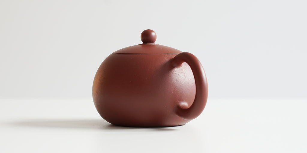 Rear view of a terracotta-colored yixing pot, highlighting the rounded handle.
