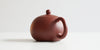 Rear view of a terracotta-colored yixing pot, highlighting the rounded handle.