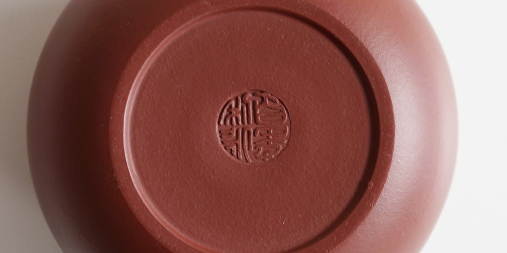 The bottom of a terracotta-colored yixing teapot. A maker’s mark is stamped into the base.