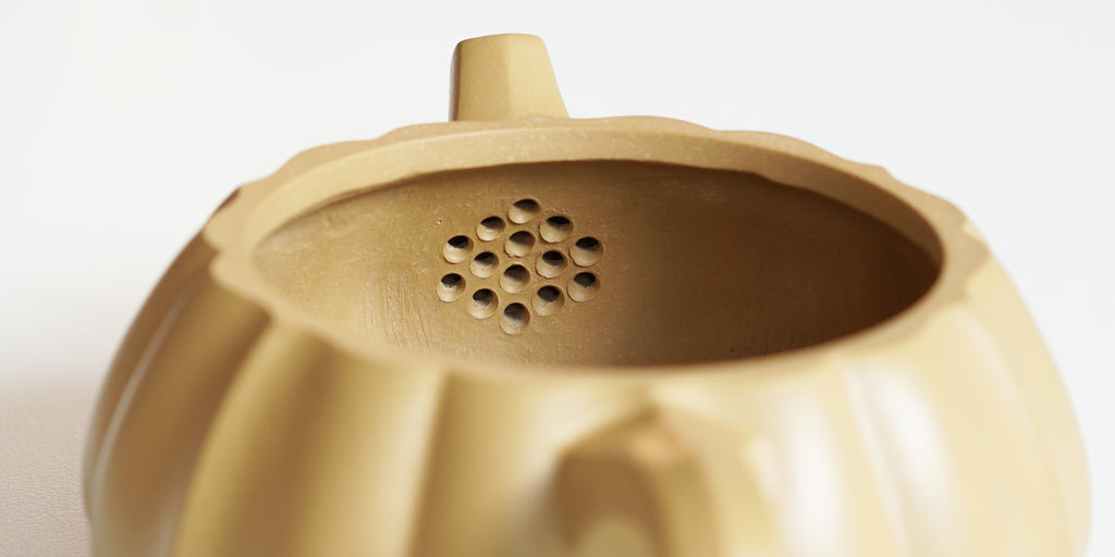 Rear view of the inside of a yellow yixing pot, showcasing the built-in filter made by punching small holes in the clay.