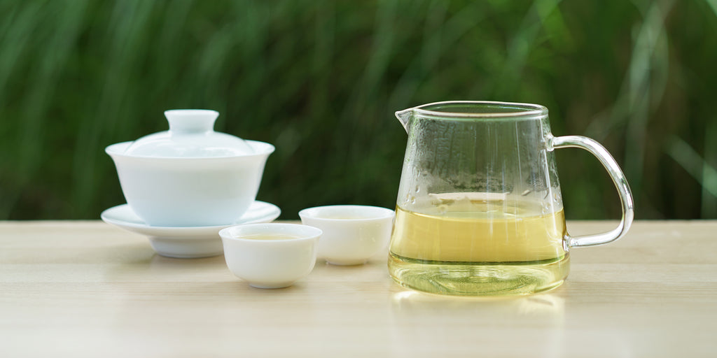 From left to right, a gaiwan, two teacups, and a glass server. The teacups and server have Formosa oolong tea in them.