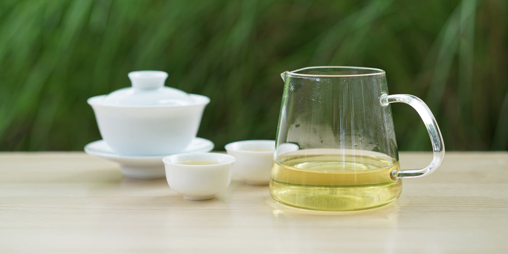 From left to right, a gaiwan, two teacups, and a glass server. The teacups and server have Formosa oolong tea in them.