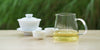 From left to right, a gaiwan, two teacups, and a glass server. The teacups and server have Formosa oolong tea in them.