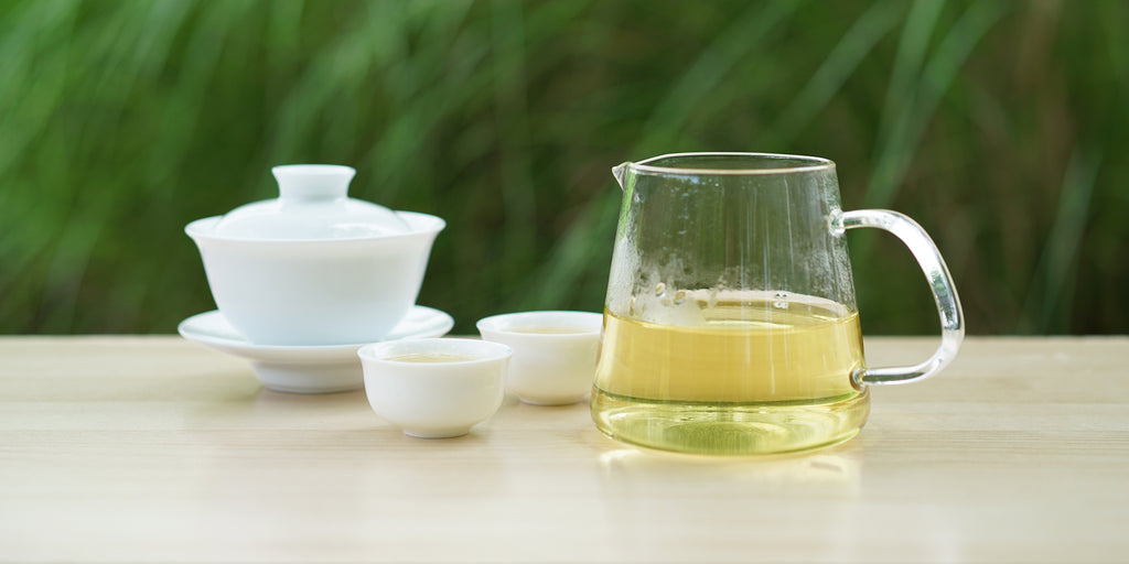 From left to right, a gaiwan, two teacups, and a glass server. The teacups and server have Formosa oolong tea in them.