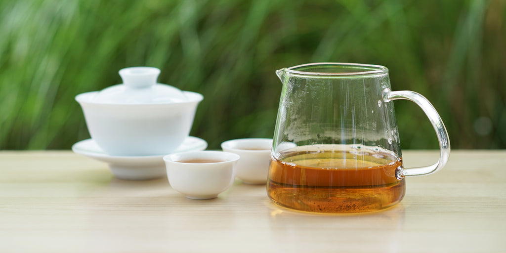 From left to right, a gaiwan, two teacups, and a glass server. The teacups and server have Formosa oolong tea in them.