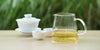 From left to right, a gaiwan, two teacups, and a glass server. The teacups and server have Formosa oolong tea in them.