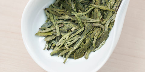 A white dish containing dry green tea leaves.
