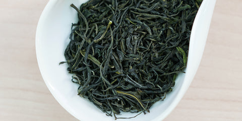A white dish containing dry green tea leaves.