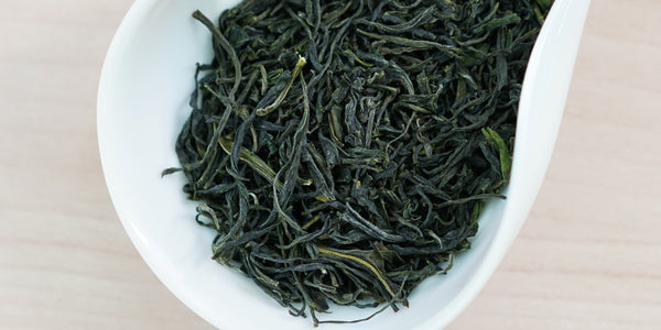A white dish containing dry green tea leaves.