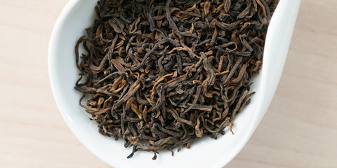 A white dish containing dry pu-erh tea leaves.