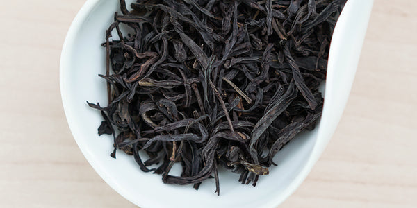 A white dish containing dry Phoenix oolong tea leaves.