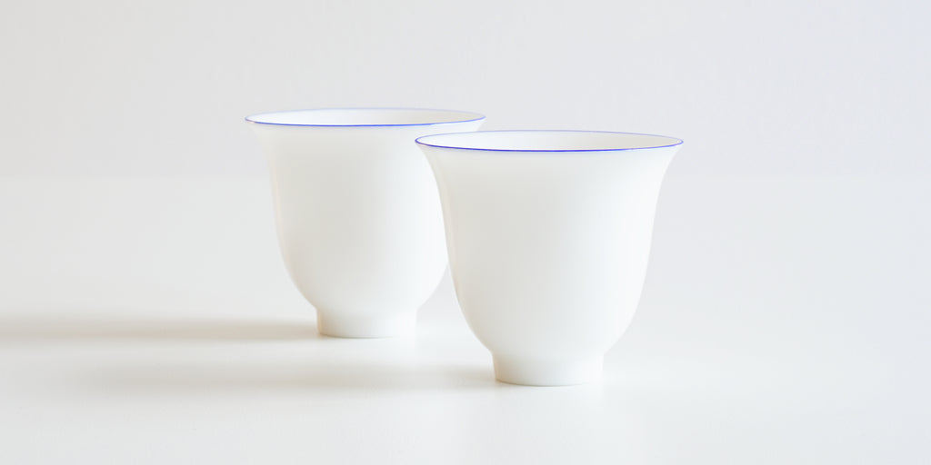 Side view of a pair of white porcelain teacups, with a ring of blue painted around the rim.