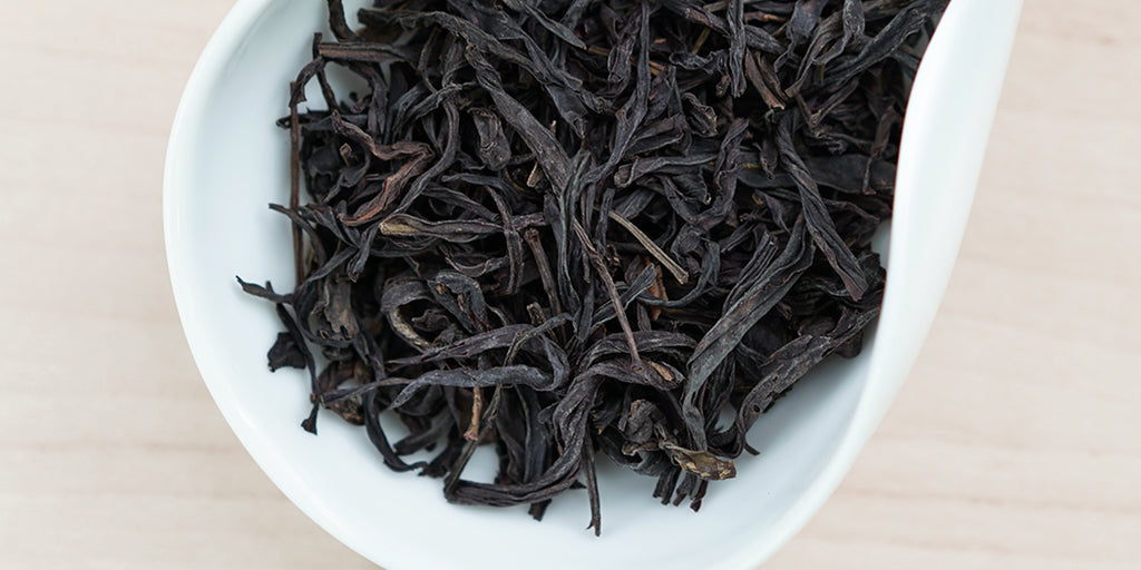 A white dish containing dry Phoenix oolong tea leaves. 