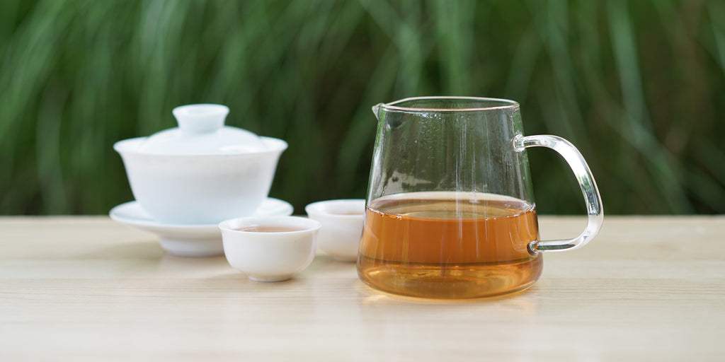 From left to right, a gaiwan, two teacups, and a glass server. The teacups and server have Phoenix oolong tea in them.