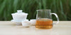 From left to right, a gaiwan, two teacups, and a glass server. The teacups and server have Phoenix oolong tea in them.