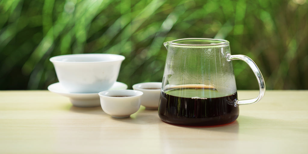From left to right, a gaiwan, two teacups, and a glass server. The teacups and server have pu-erh tea in them.