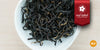 A white dish containing dry black tea leaves. A red ribbon in the top right corner reads “Red Label Collection”, and an orange circle in the bottom right corner reads “MX”