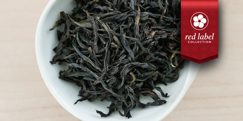 A white dish containing dry Phoenix oolong tea leaves. A red ribbon in the top right corner reads “Red Label Collection”