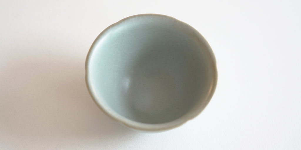 Top down view of a blue-green celadon teacup. The lip has slight indentations from the grooves on the outside.