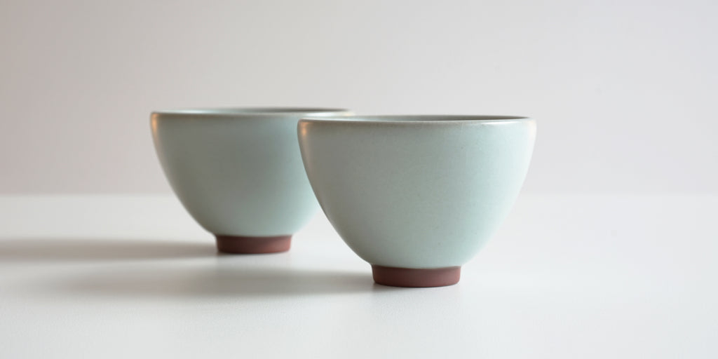 Side view of a pair of blue-green celadon teacups.