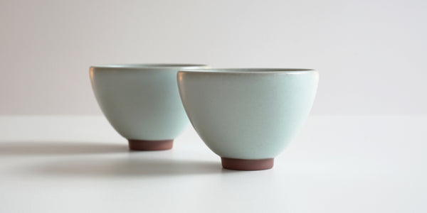 Side view of a pair of blue-green celadon teacups.