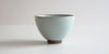 Side view of a blue-green celadon teacup, showing the oval shape and unglazed foot.