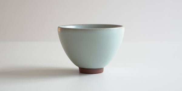 Side view of a blue-green celadon teacup, showing the oval shape and unglazed foot.