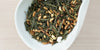 A white dish containing dry green tea leaves and toasted rice.