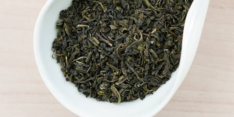 A white dish containing dry jasmine tea leaves.