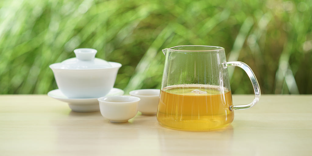 From left to right, a gaiwan, two teacups, and a glass server. The teacups and server have jasmine tea in them.