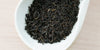 A white dish containing dry black tea leaves.