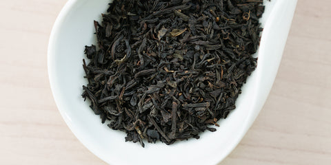 A white dish containing dry black tea leaves.