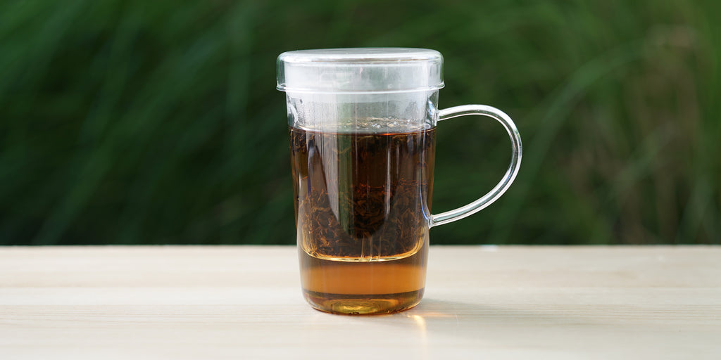 A glass cup with lapsang souchong brewing in the nested glass infuser.