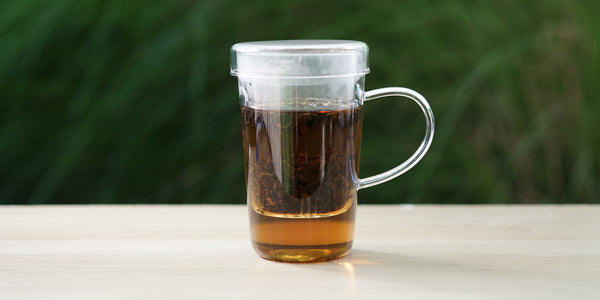 A glass cup with lapsang souchong brewing in the nested glass infuser.