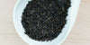 A white dish containing dry black tea leaves.