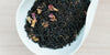 A white dish containing dry black tea leaves and rose petals