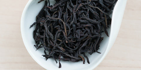 A white dish containing dry Phoenix oolong tea leaves.