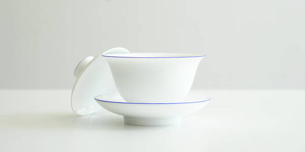 Side view of the gaiwan, with the lid off kilter resting on its side against the bowl.