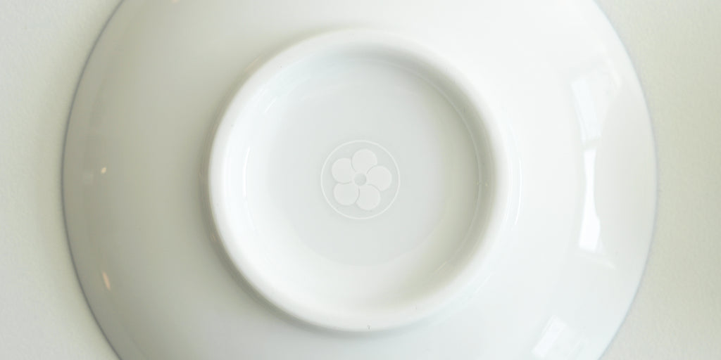 The bottom of a white dish, with Red Blossom Tea Company’s logo etched in white into the bottom of the foot.