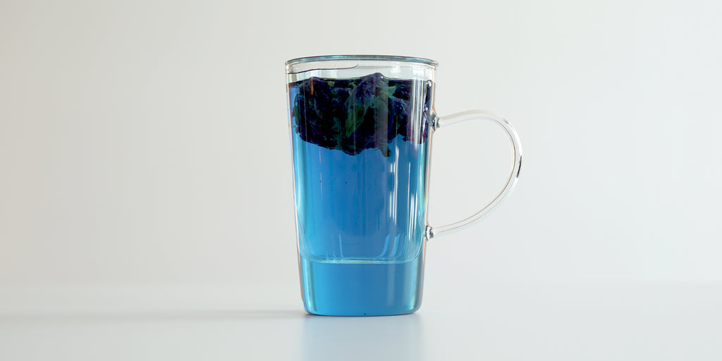 A glass cup with butterfly pea flowers brewing in a nested glass infuser, floating to the top.
