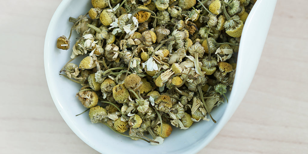 A white dish containing dry chamomile flowers.