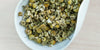 A white dish containing dry chamomile flowers.
