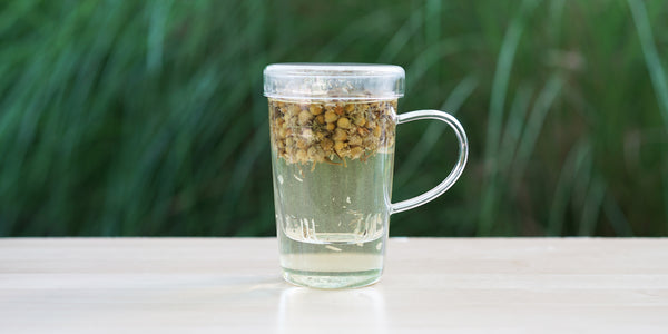 A glass cup with chamomile flowers brewing in the nested glass infuser.