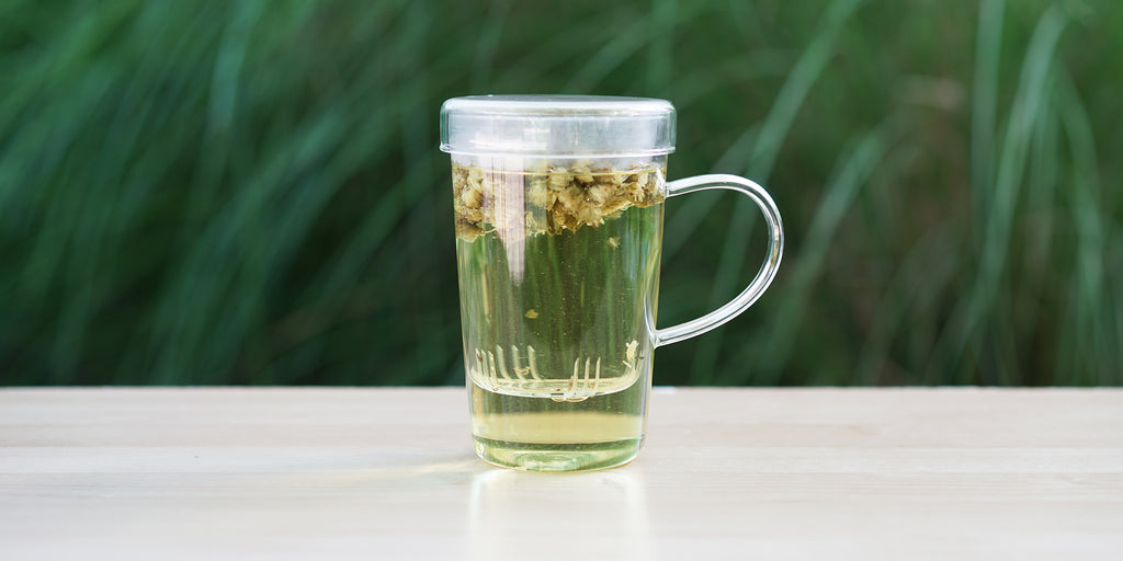 A glass cup with chrysanthemum buds brewing in the nested glass infuser.