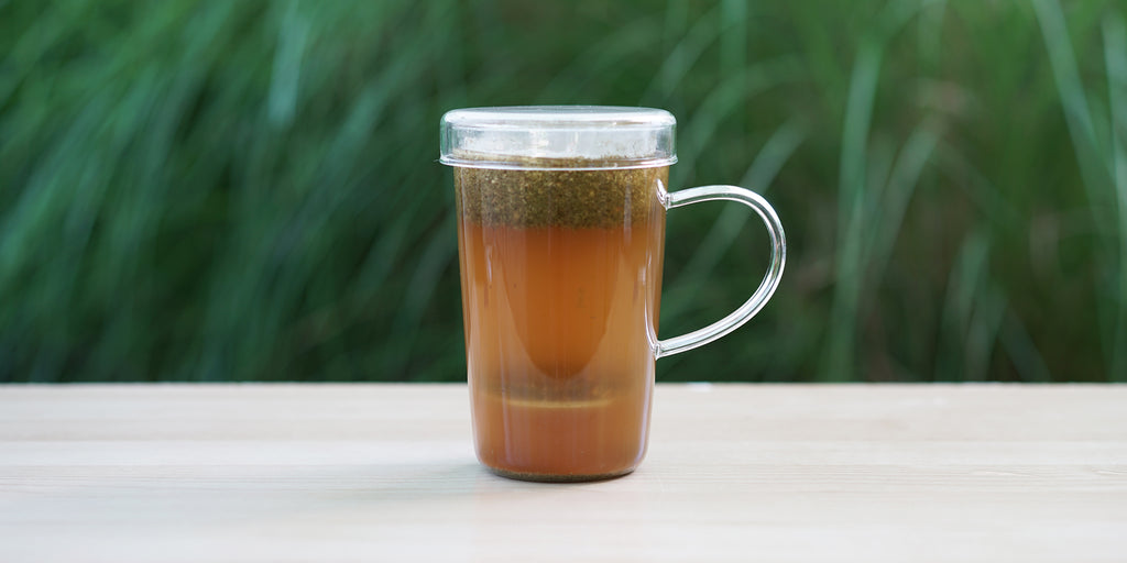 A glass cup with ginger lemongrass brewing in the nested glass infuser.