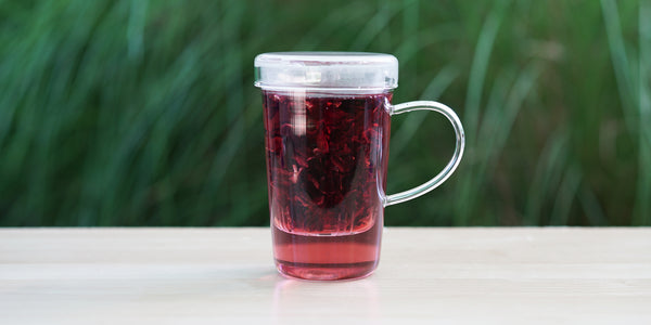 A glass cup with hibiscus brewing in the nested glass infuser.