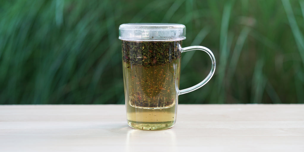 A glass cup with peppermint rose brewing in the nested glass infuser.