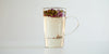 A glass cup with rose buds brewing in a nested glass infuser, floating to the top.