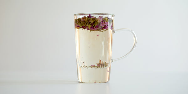 A glass cup with rose buds brewing in a nested glass infuser, floating to the top.