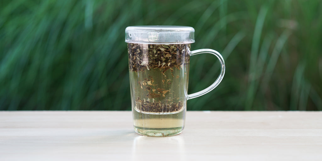A glass cup with wild guava leaves brewing in the nested glass infuser.
